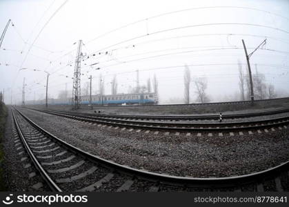 The Ukrainian suburban train rushes along the railway in a misty morning. Fisheye photo with increased distortion