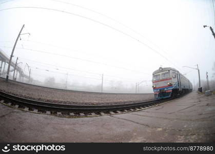 The Ukrainian suburban train rushes along the railway in a misty morning. Fisheye photo with increased distortion