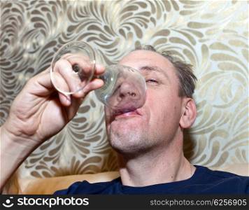 The unshaven man finishes drinking the last drink of alcohol from a glass