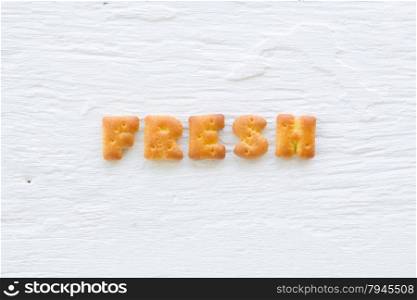 The upper-case letters word FRESH. Alphabet cookie crackers putting on rough texture of white wood background.