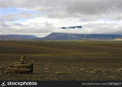 The vast, barren tundra landscape of the Sprengisandur Highland Road in Iceland, with the huge Vatnajokull volcanic glacier visible through the clouds.