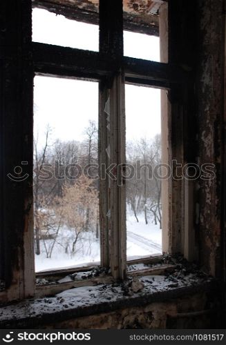 the view from the window of the burnt old building in winter time. Trees and snow outside.