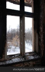 the view from the window of the burnt old building in winter time. Trees and snow outside.