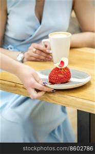 The waiter&rsquo;s hand puts on the table a plate with a red cupcake on the background of a female client in a cafe. Waiter puts on table cupcake