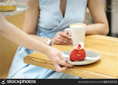 The waiter&rsquo;s hand puts on the table a plate with a red cupcake on the background of a female client in a cafe. Waiter puts on table cupcake