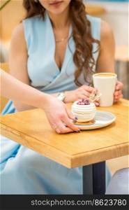 The waitress’s hand puts the piece of cupcake on the table at a cafe, woman hand is putting round little pastry on the table on a background of a female in a blue dress. Waitress puts pastry on table