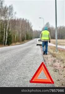 The warning triangle, mid adult man wearing reflector vest and he goes back to the his vehicle