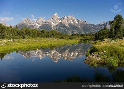 The water is perfectly smooth showing high peak reflections in the Teton&rsquo;s