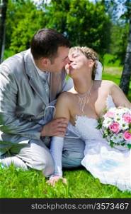 The wedding pair sits on a grass kiss