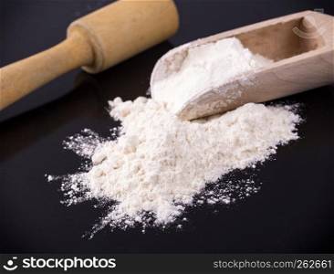 The white flour with a rolling pin on black metal background