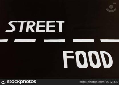 the white letters that form the written english street food are positioned in the two lanes of a road