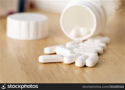 The white pills are by the medicine bottle on wooden table. Set of white pills are by the medicine bottle
