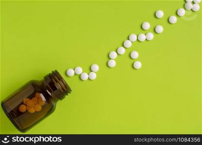 The white pills are scattered on a green background. Glass medicinal bottle. Top view. The white pills are scattered on a green background. Glass medicinal bottle.