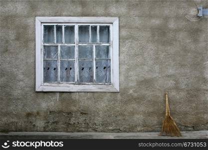 The window of the old house and the broom against the wall