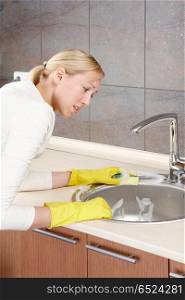 The woman discontentedly cleans a bowl on kitchen. The cleaner