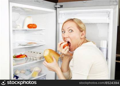 The woman greedy eats meal against an open refrigerator. Terrible hunger