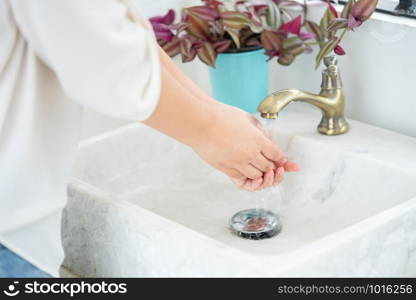 The woman hand is going to open the faucet to wash hands. To maintain cleanliness after entering the bathroom, the concept of health and cleanliness.