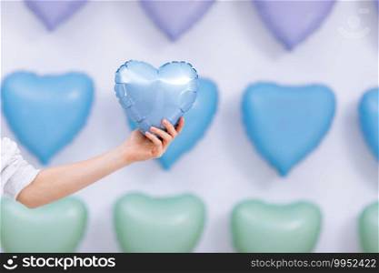 The woman holds the blue balloon in the form of a heart on many hearts background. valentines day. selective focus.. The woman holds the blue balloon in the form of a heart on many hearts background. valentines day. selective focus