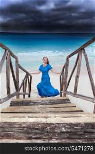 The woman in a long blue dress goes on the stormy sea coast