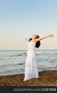 The woman in a white sundress on seacoast with open hands. A picturesque landscape