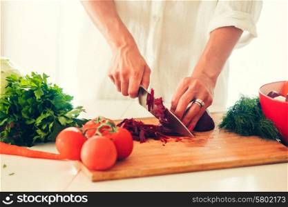 The woman is cooking at the kitchen ( slicing vegetables )