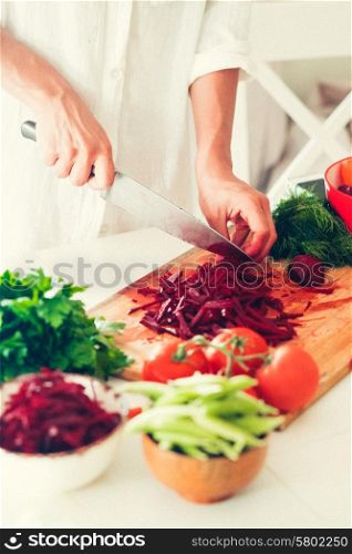 The woman is cooking at the kitchen ( slicing vegetables )