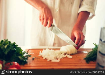 The woman is cooking at the kitchen ( slicing vegetables )