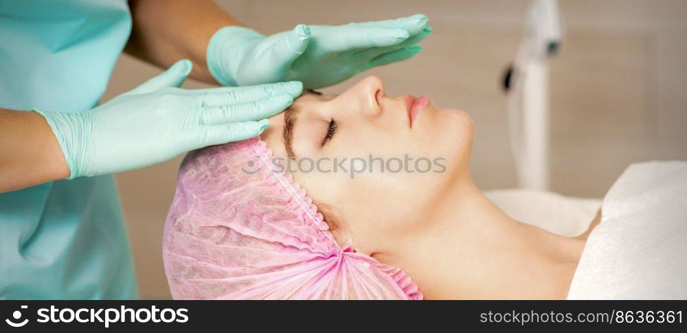 The woman is having cosmetic treatment during cosmetologist in medical gloves are touching the female face at the spa salon. The woman is having cosmetic treatment during cosmetologist in medical gloves are touching the female face at the spa salon.