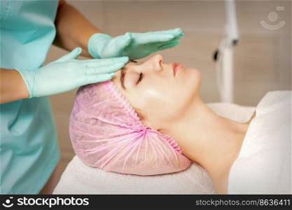 The woman is having cosmetic treatment during cosmetologist in medical gloves are touching the female face at the spa salon. The woman is having cosmetic treatment during cosmetologist in medical gloves are touching the female face at the spa salon.