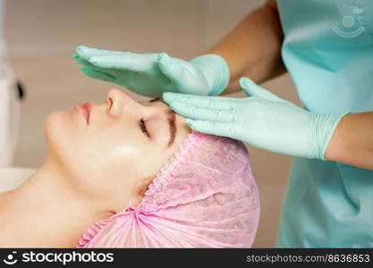 The woman is having cosmetic treatment during cosmetologist in medical gloves are touching the female face at the spa salon. The woman is having cosmetic treatment during cosmetologist in medical gloves are touching the female face at the spa salon.