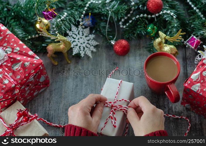 The woman is holding a gift package in hand on the wooden table.Christmas decoration with ornaments