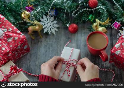 The woman is holding a gift package in hand on the wooden table.Christmas decoration with ornaments