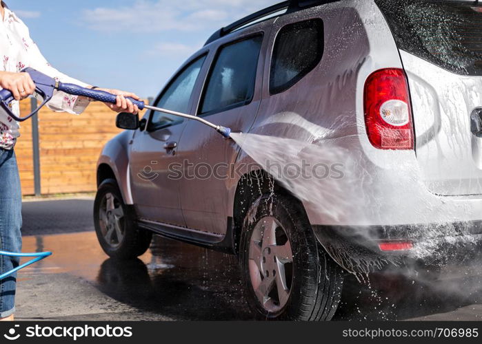 The woman is holding a lance in her hand and washes her car under high pressure with water and shampoo