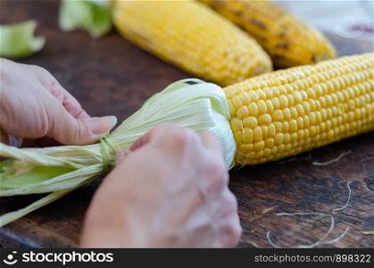 The woman is peeling corn shells on dark wooden table.