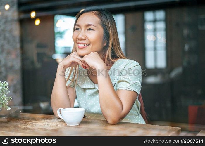 The woman is sitting in a coffee shop, putting the chin on the back of the hand and having a cup of coffee.