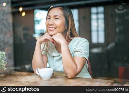 The woman is sitting in a coffee shop, putting the chin on the back of the hand and having a cup of coffee.