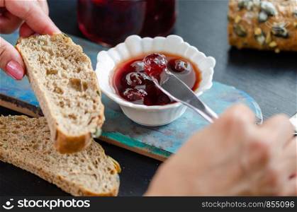 The woman is taking sour cherry jam on her bread.