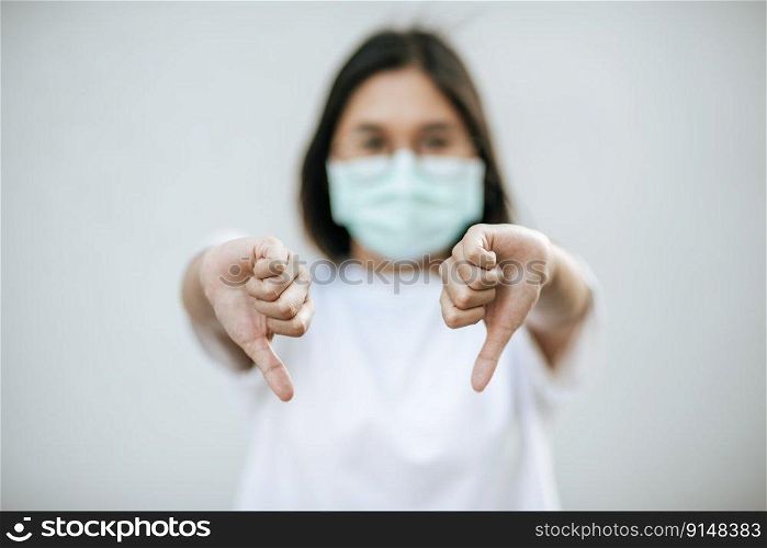 The woman is wearing a mask and pointing her thumb down.