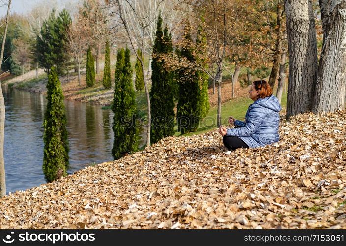 The woman is yoga meditating and making zen symbol on autumn leaves on the outdoors.