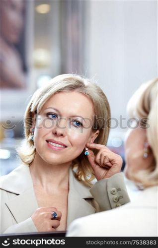 The woman of middle age tries on earrings at a mirror