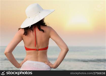 The woman on sea coast in a hat. Sunset illumination.The up view