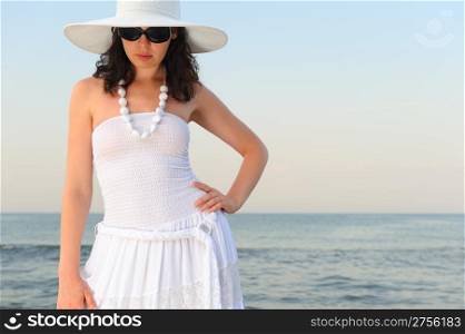 The woman on seacoast. In sun glasses, a sundress, a hat.