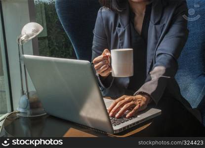 The woman's hand is working on the laptop.And the right hand holding a coffee mug to drink on her table