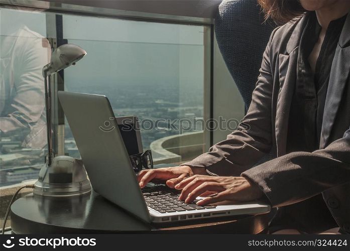 The woman?s hand is working with a laptop and has a light bulb. Glasses on the desk