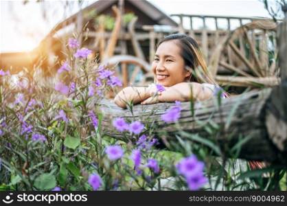 The woman sat happily in the flower garden and laid her hands and towards the wooden fence.