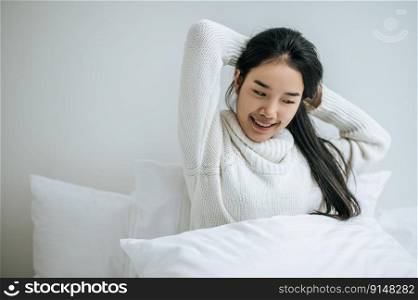 The woman sits on the bed with both hands raised.