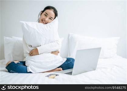 The woman sitting on the bed and hugging laptop. Selective focus.