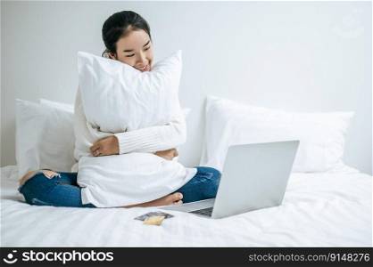 The woman sitting on the bed and hugging laptop. Selective focus.