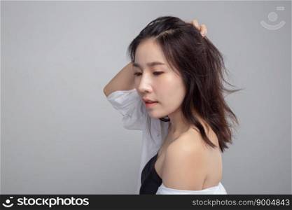 The woman wears a white shirt and hands touch her hair.