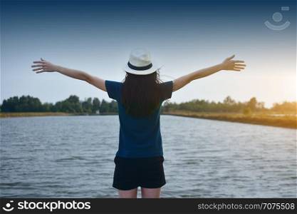 The woman wore a white T-shirt and a hat, standing on the river and the two hands on the sky.